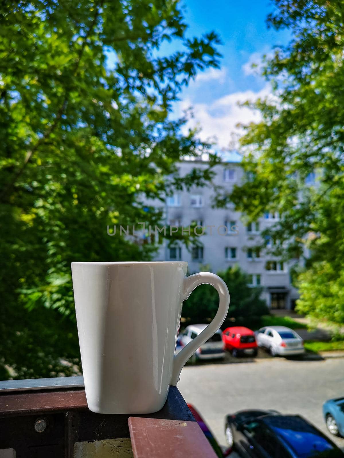 White cup of coffee standing on edge of balcony railing by Wierzchu