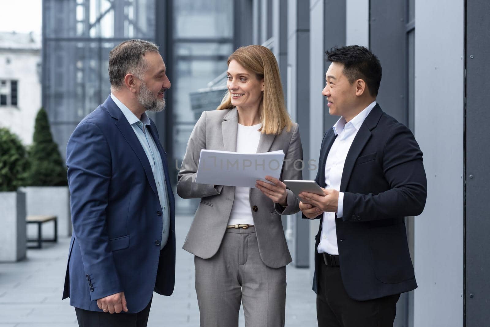 International business team meeting mature man, Caucasian woman, Asian employee communicate . group of entrepreneurs in formal suits discuss a project document near office center on street