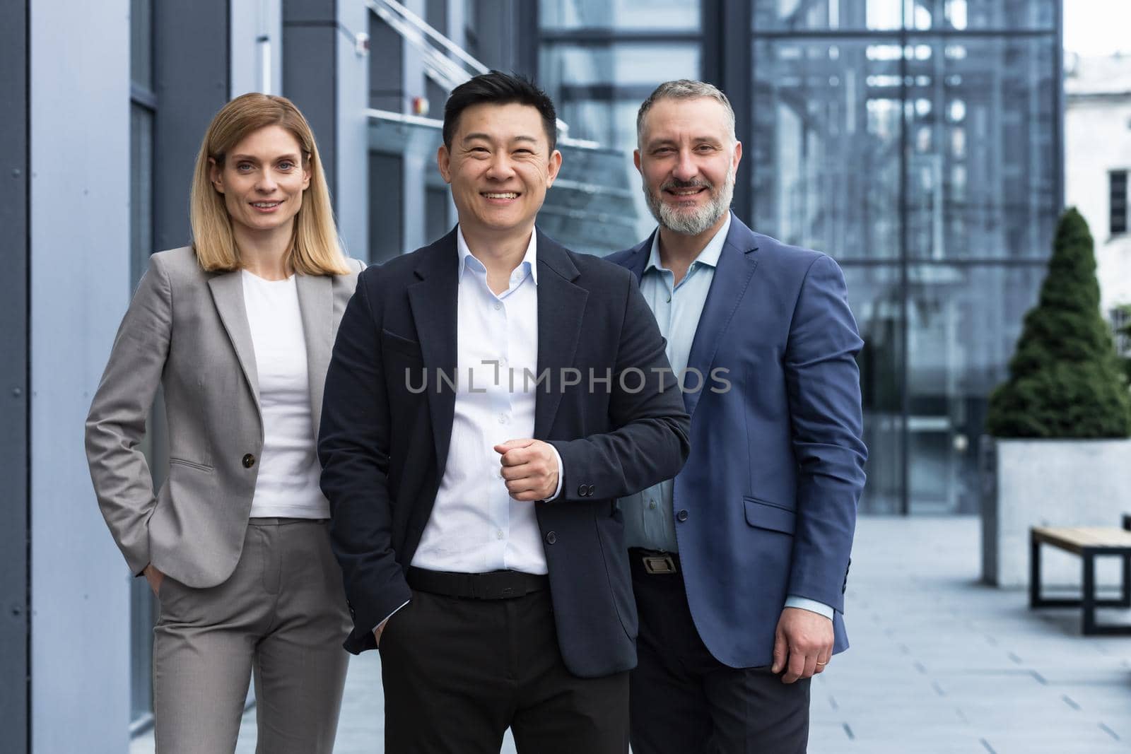 Successful diverse business team, three workers smiling and looking at camera, dream team with asian boss outside office building, colleagues in business suits