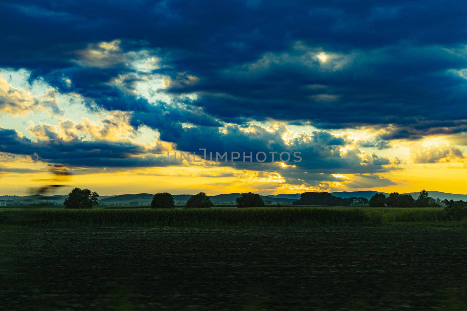 Beautiful shining sun behind big clouds at sunset over big fields