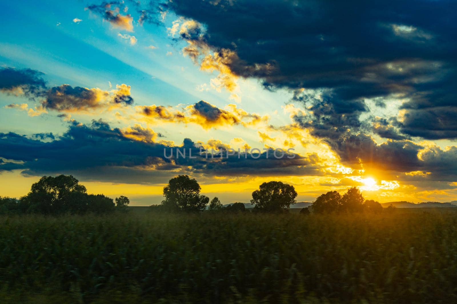 Beautiful shining sun behind big clouds at sunset over big fields