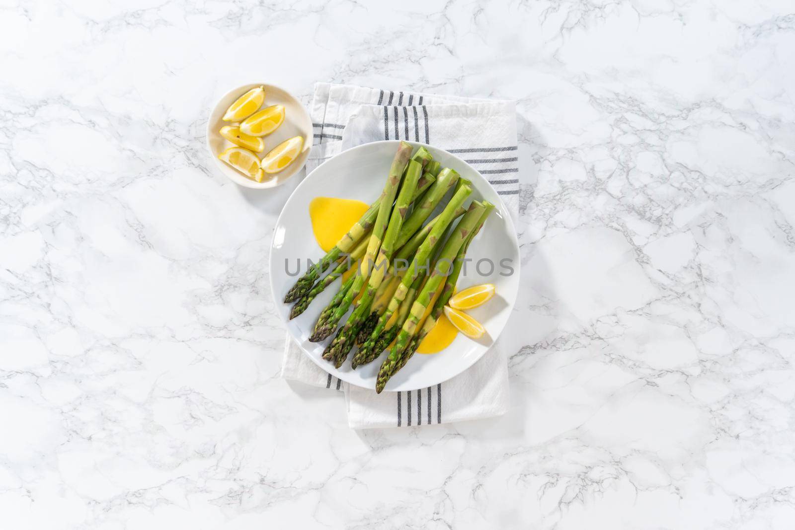 Flat lay. Serving steamed asparagus with homemade hollandaise sauce with lemon wedges on a white plate.