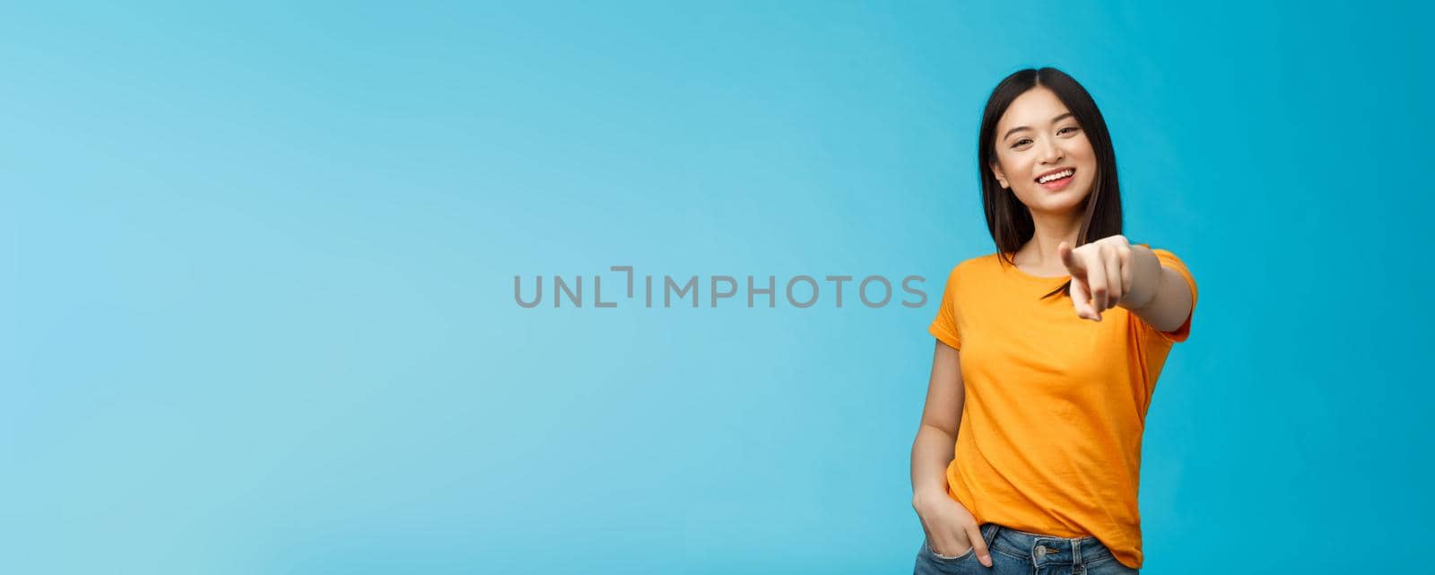 Lucky winner. Cheerful charismatic asian cute urban girl stand yellow t-shirt smiling friendly pointing finger camera choosing, picking person, inviting you team, stand happy blue background.