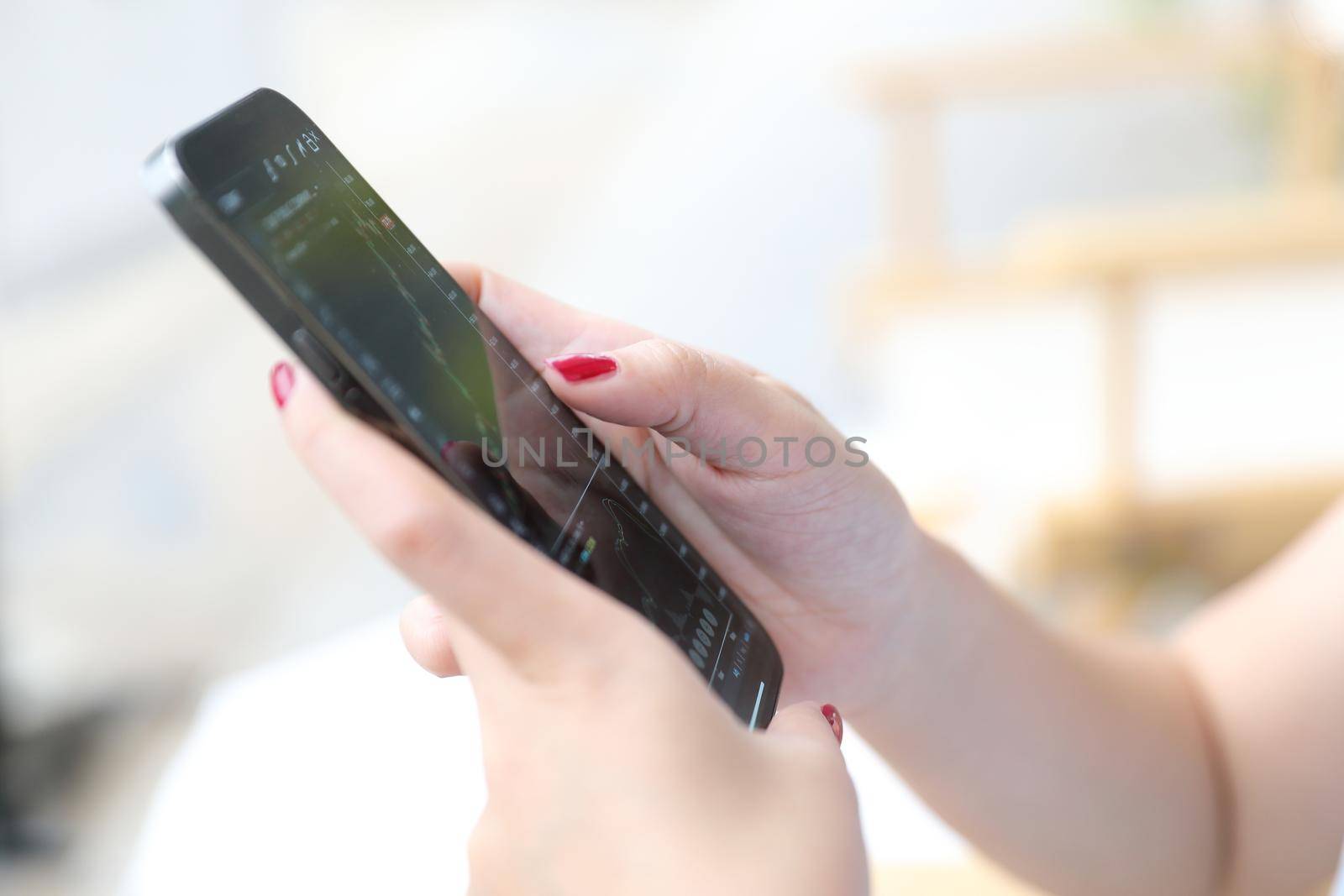 Female hand with smartphone trading stocks online in coffee shop Business concept by piyato