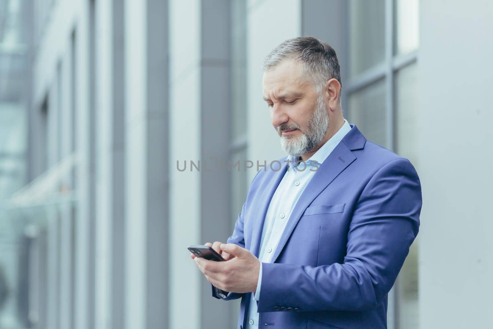 Close-up photo. Senior gray-haired man, a businessman calls a taxi from the phone,waits by voronaman