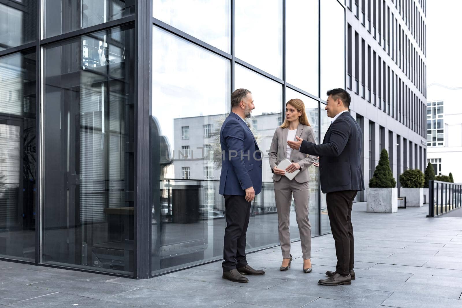 Meeting of three successful business people, diverse dream team man and woman outside office building, greeting and shaking hands, experienced professionals specialists in business suits talking