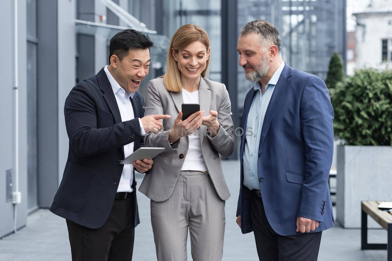 Three colleagues employees watch funny videos or look at photos, pictures memories looking at smartphone screen using mobile phone. group of business people office workers having fun on breaks