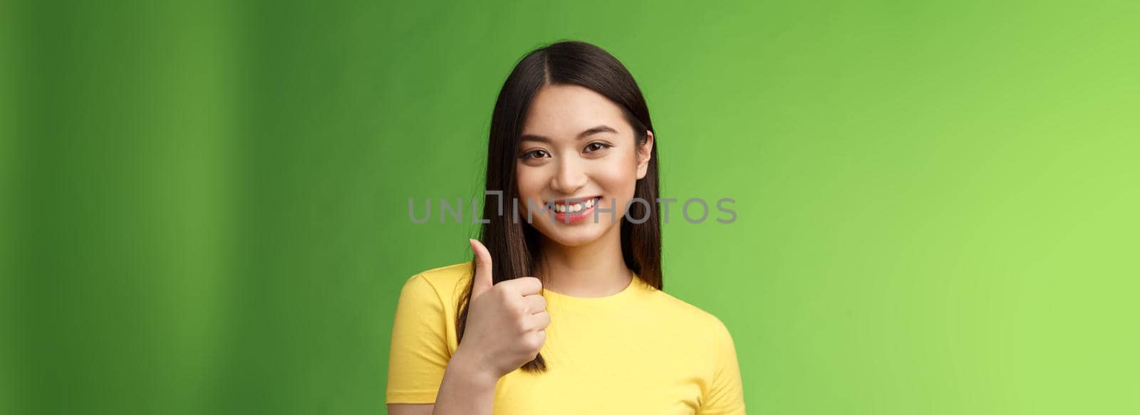 Close-up happy motivated good-looking asian woman give thumb-up smiling, approving excellent effort, like good choice, accept terms, recommend product, like idea, green background. Copy space