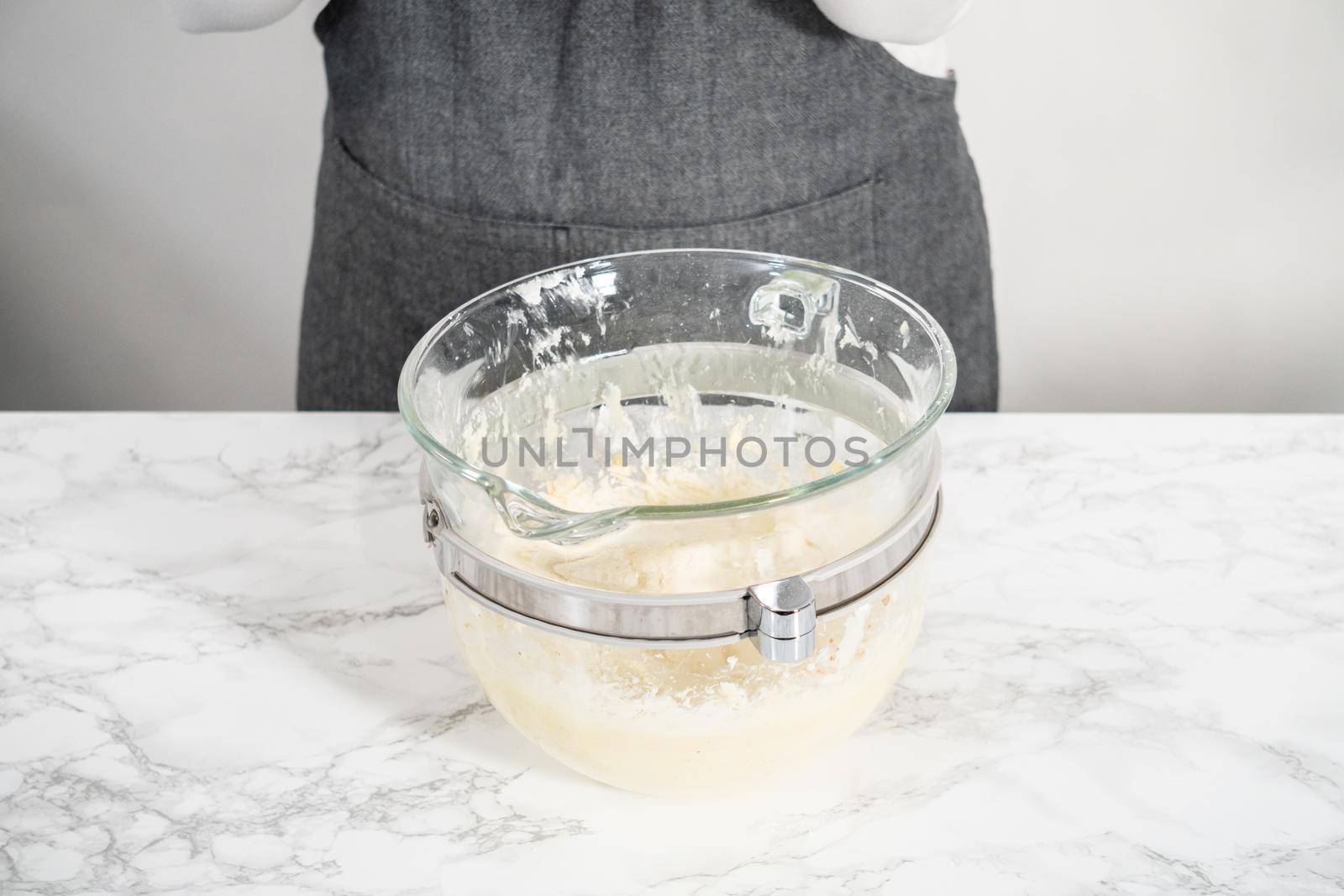 Mixing ingredients in a large glass mixing bowl of kitchen mixer to make eggnog buttercream frosting.