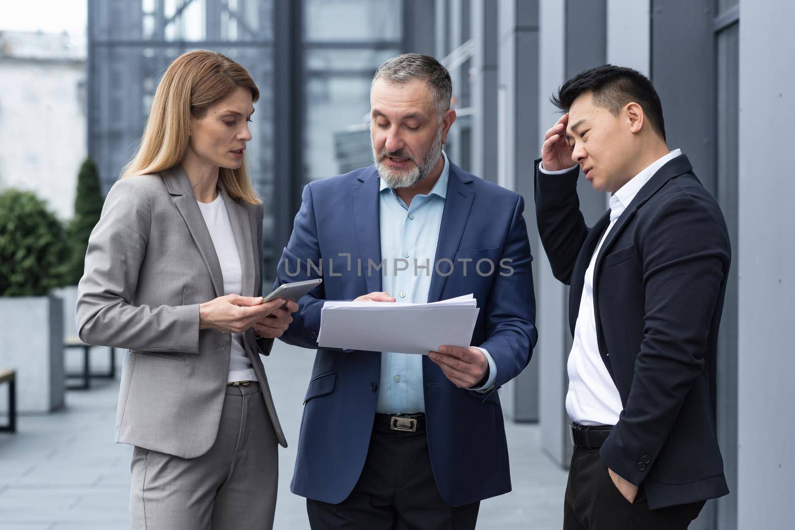 Diverse business group of three colleagues workers, upset and disappointed, result of financial report and contract document, business workers outside office building in business suits talking.