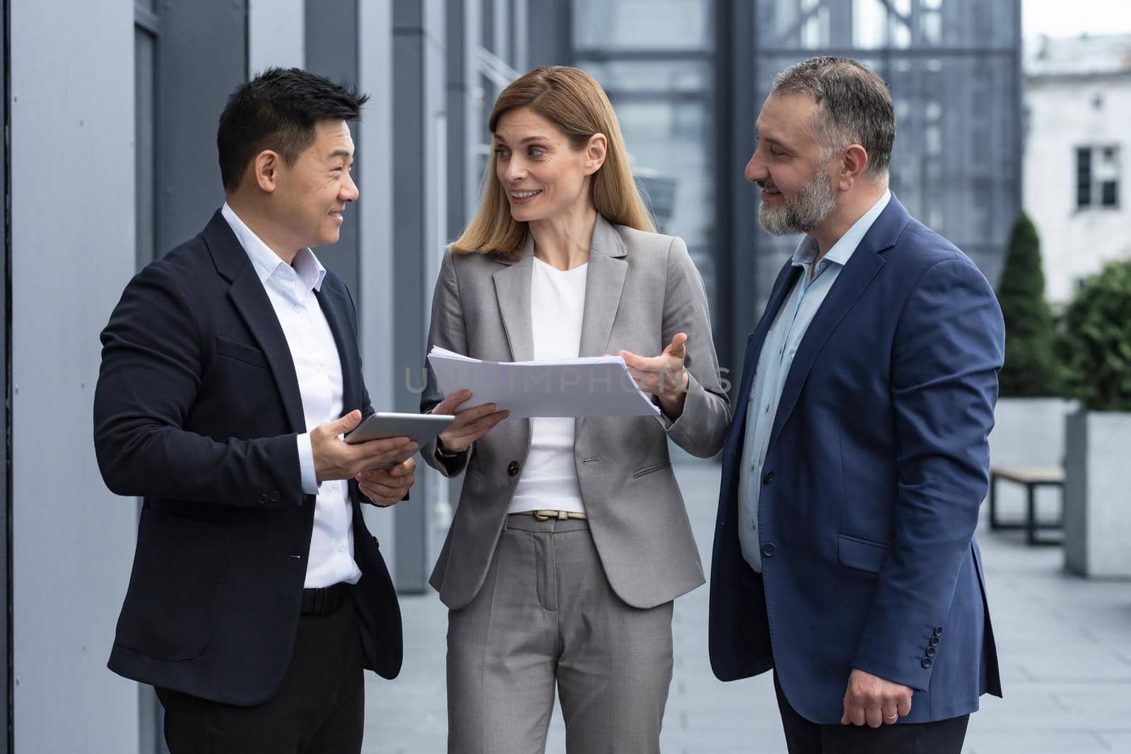 Three businessmen outside office building with documents discussing plans by voronaman