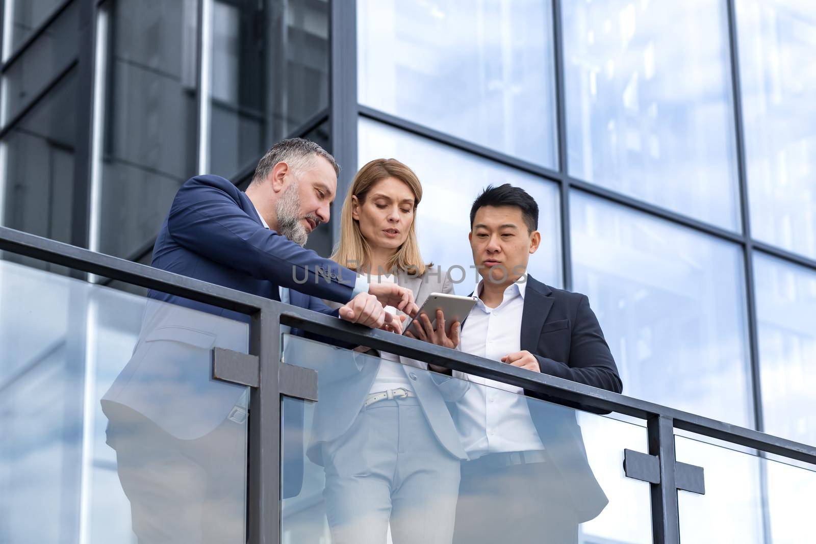 Specialist IT team leaders, group of business people outside office building, discussing and talking, testing new app on tablet, professional colleagues in business clothes,