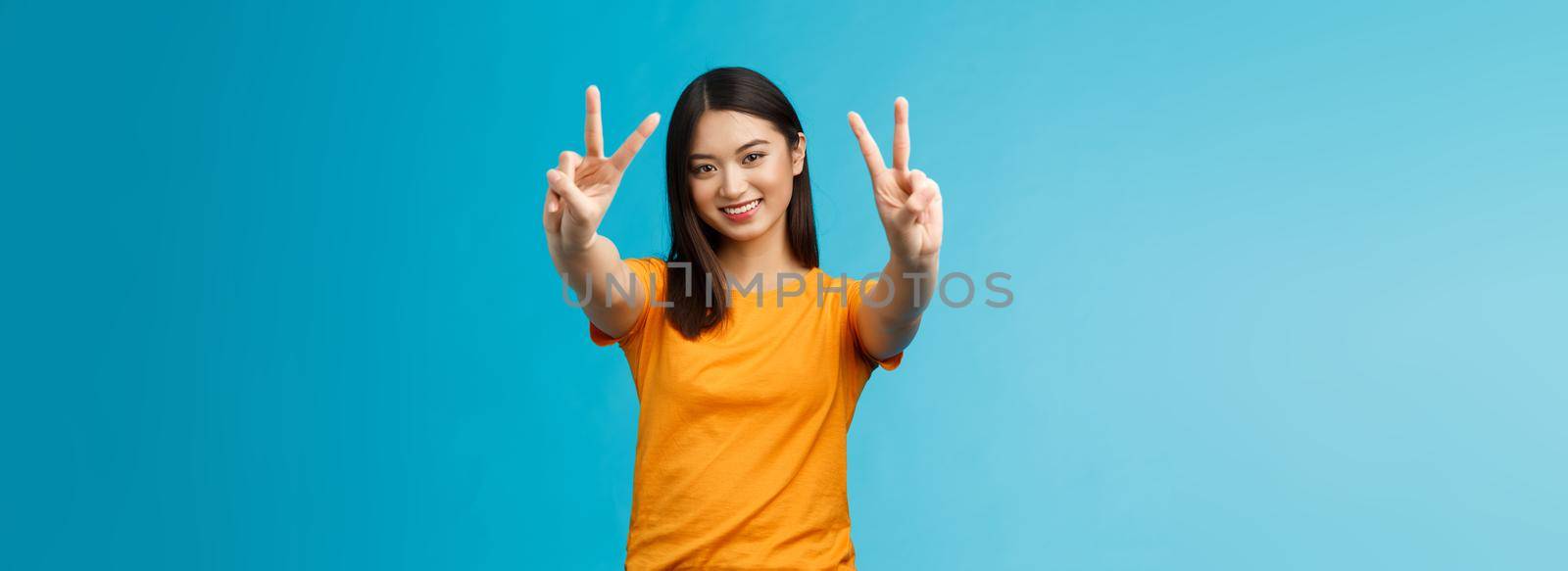 Positive upbeat cute asian girl believe win, aim success extend hands show victory, peace sign smiling broadly, have happy enthusiastic mood, spend carefree vacation travel abroad value pacifism.