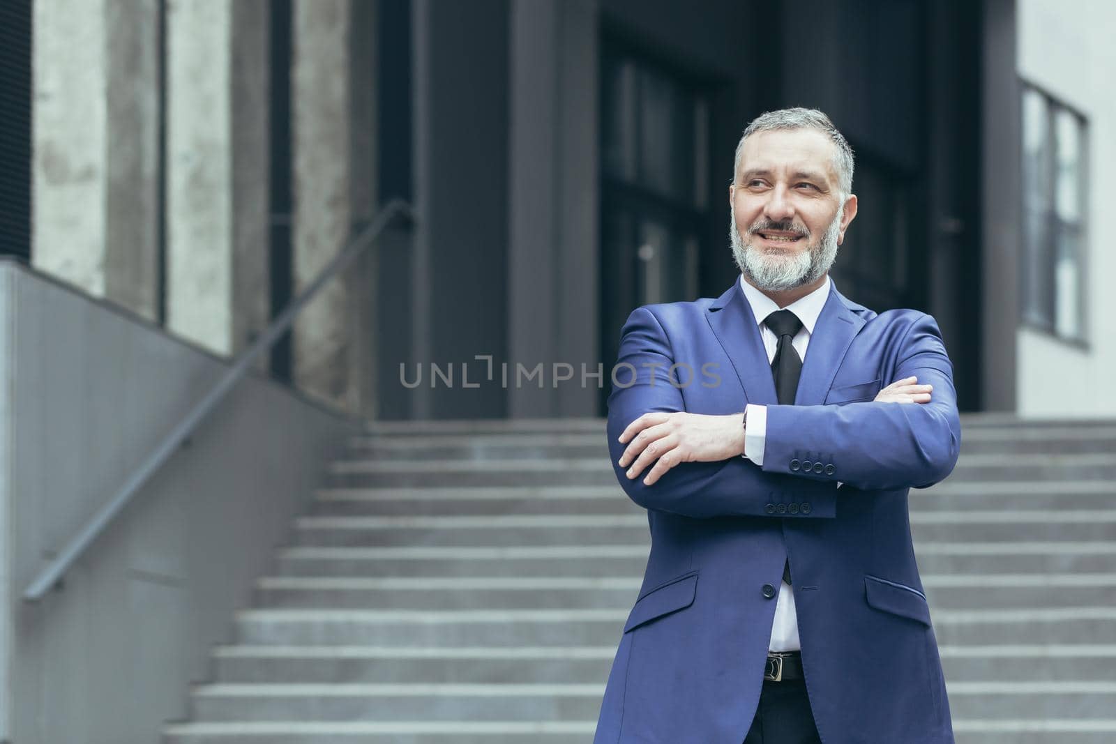 Portrait of senior handsome real estate agent man. He stands next to a business suit near a modern building, looks to the side, smiles