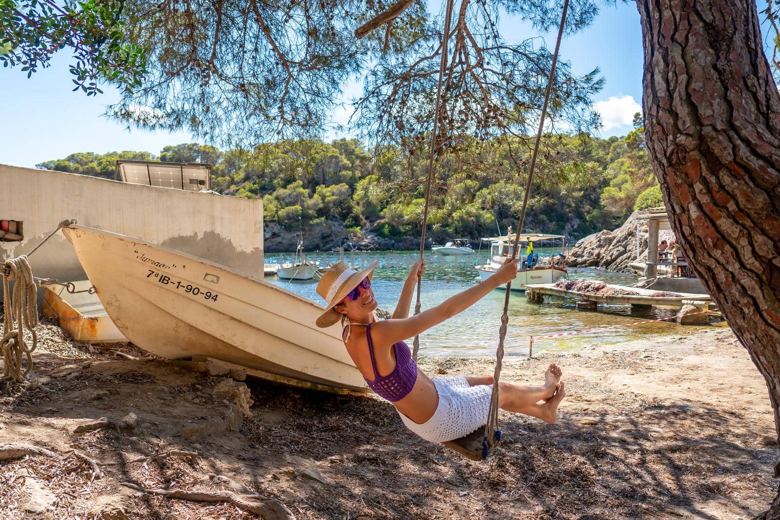 Woman on a swing on the shore of a Mediterranean cove by LopezPastor