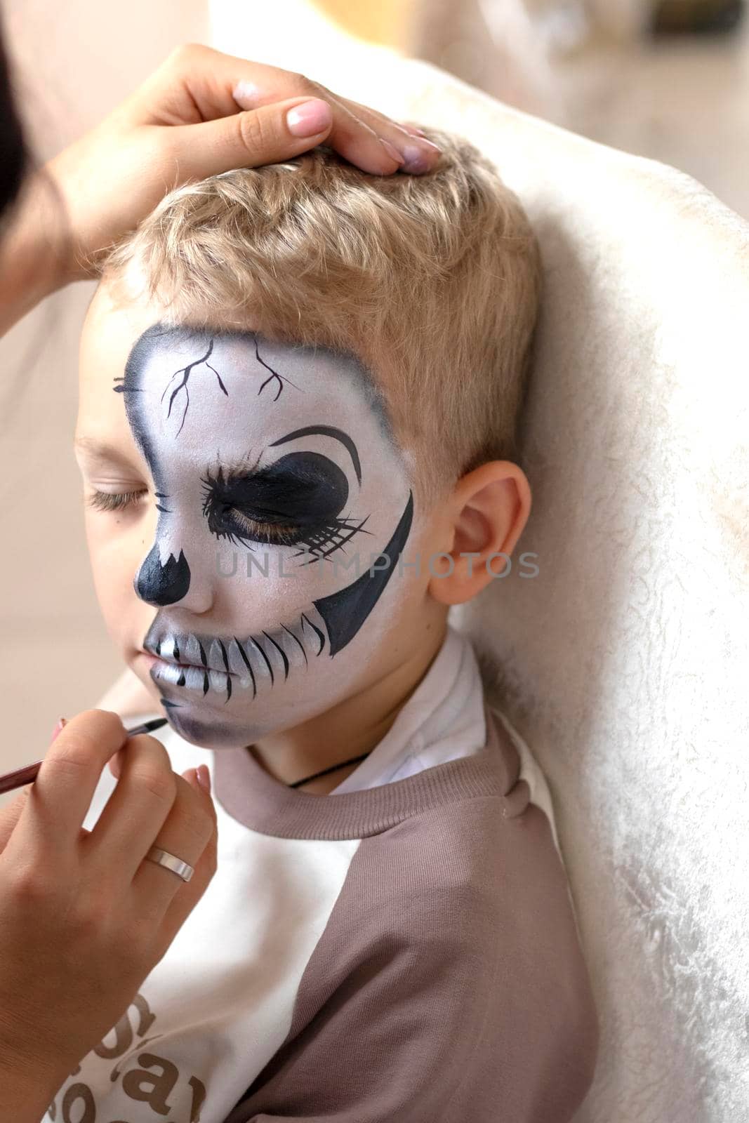 A makeup specialist girl makes a festive creepy makeup for a boy for the Halloween holiday in the studio. Happy Halloween concept. High quality photo