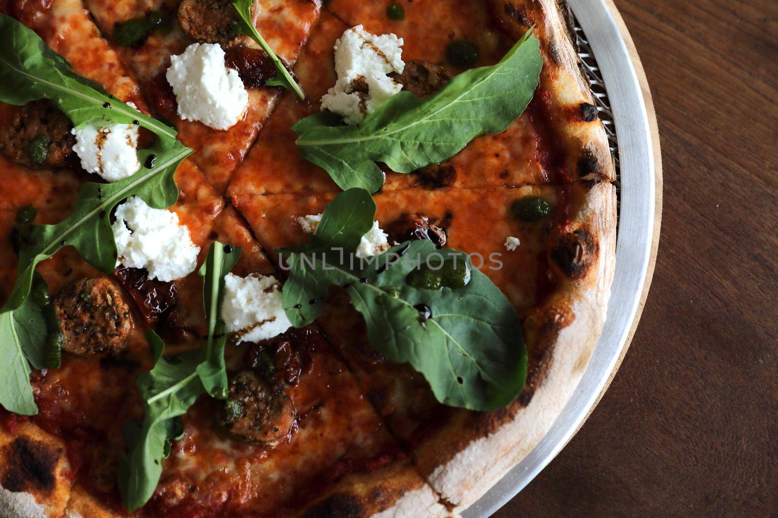 Italian Sausage and rocket salad pizza on wood background