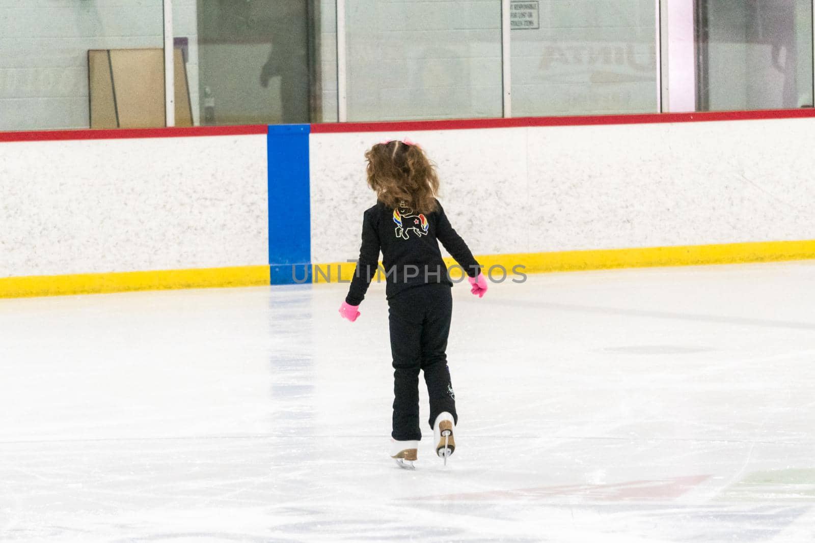 Little girl practicing figure skating moves on the indoor ice rink.