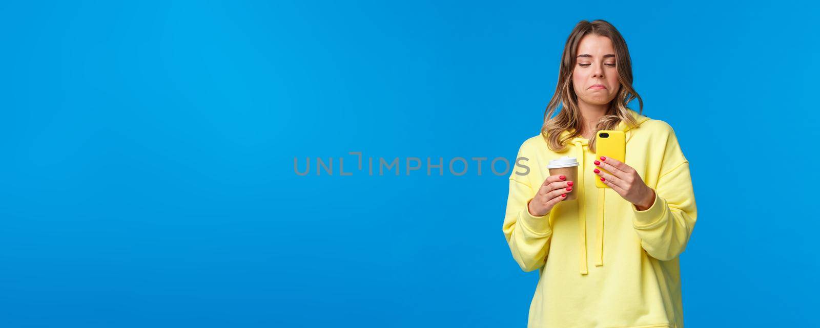 Girl checking out her photo on smartphone screen with not bad expression, look pleased and not in approval after editing pic in mobile application, drinking coffee from paper cup by Benzoix