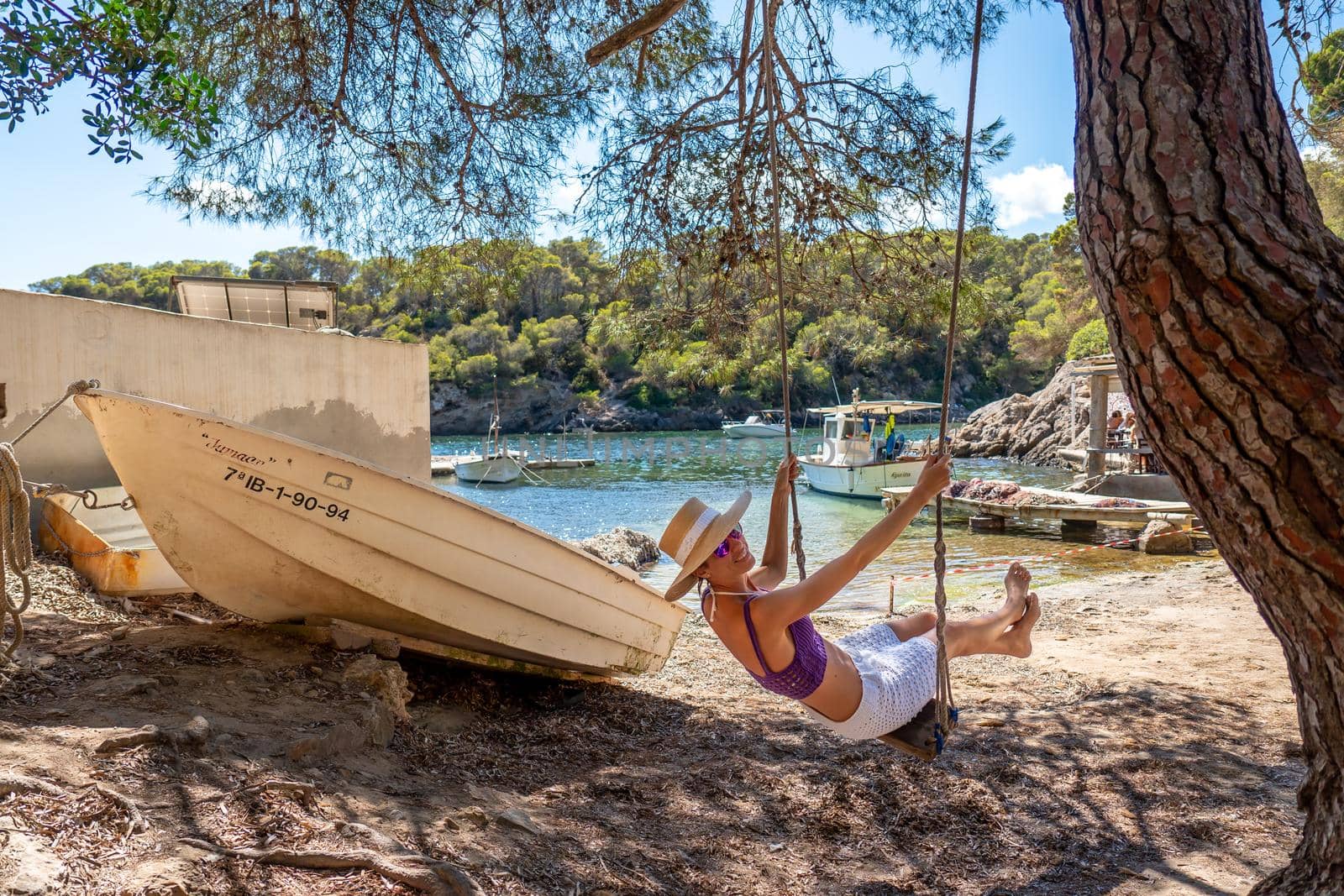 Woman on a swing on the shore of a Mediterranean cove by LopezPastor