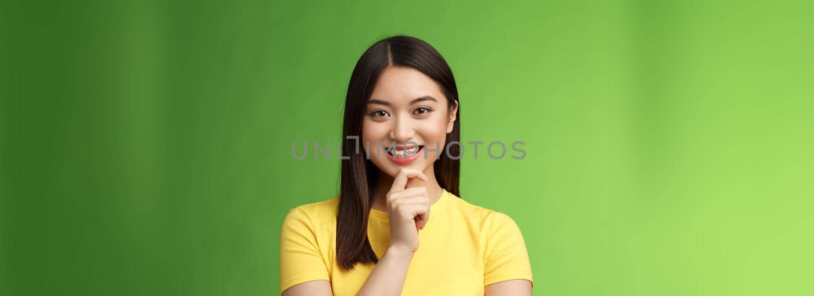 Smart assertive creative asian female student make interesting research assumption, smiling intrigued touch chin thoughtful, have good plan idea, thinking, ponder choices, green background.