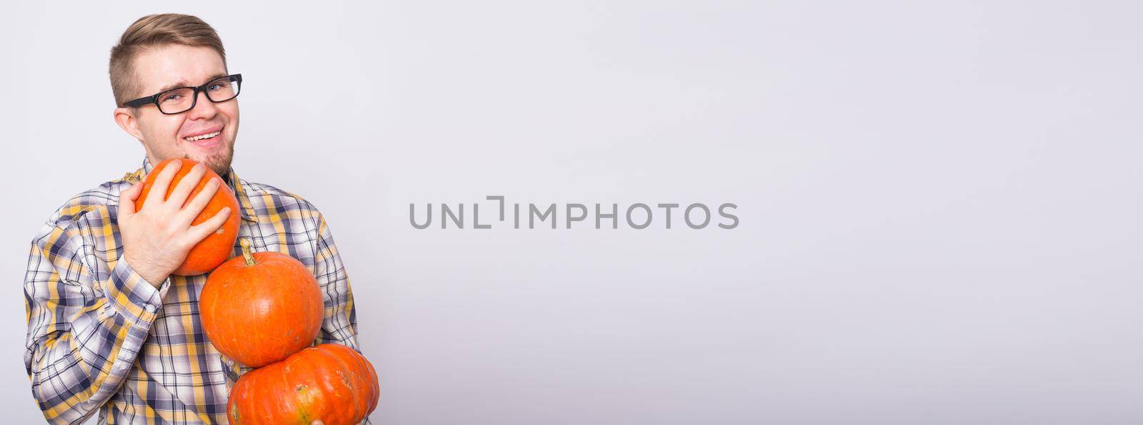 Harvesting, halloween and people concept - Man in black glasses holding three pumpkins over white background.