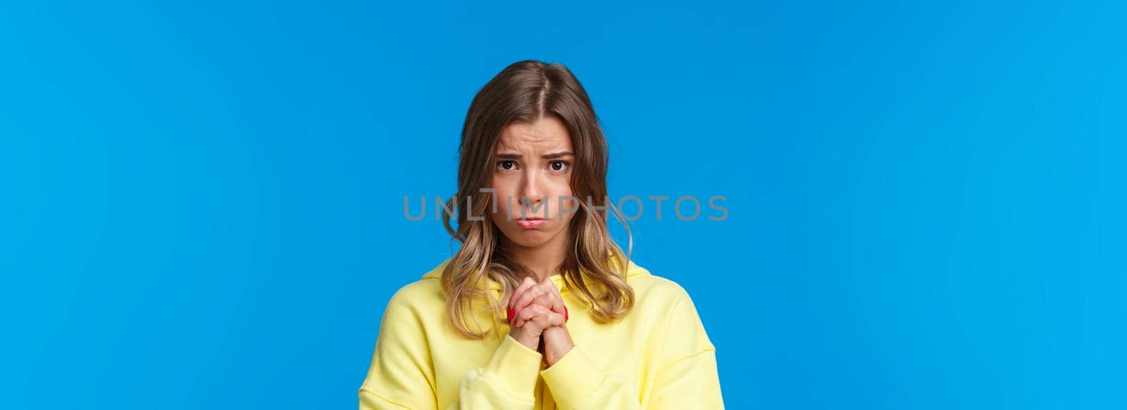 Close-up portrait of innocent cute and silly sulking girl with blond hair begging for help, hold hands in supplication pray gesture, frowning asking favour, need something and pleading.