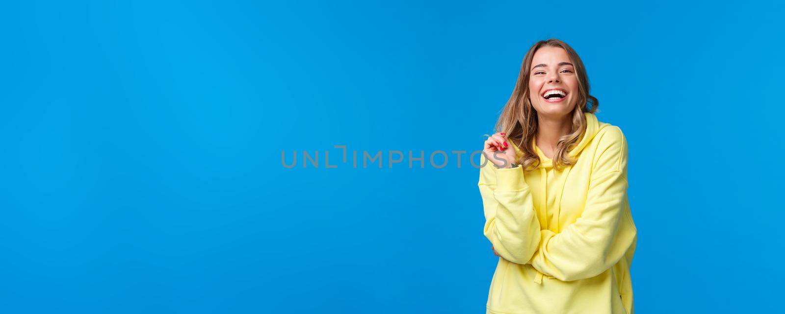 Happy blond young girl laughing from funny joke, having conversation with friends standing near university campus enjoying being in hilarious company, standing blue background.