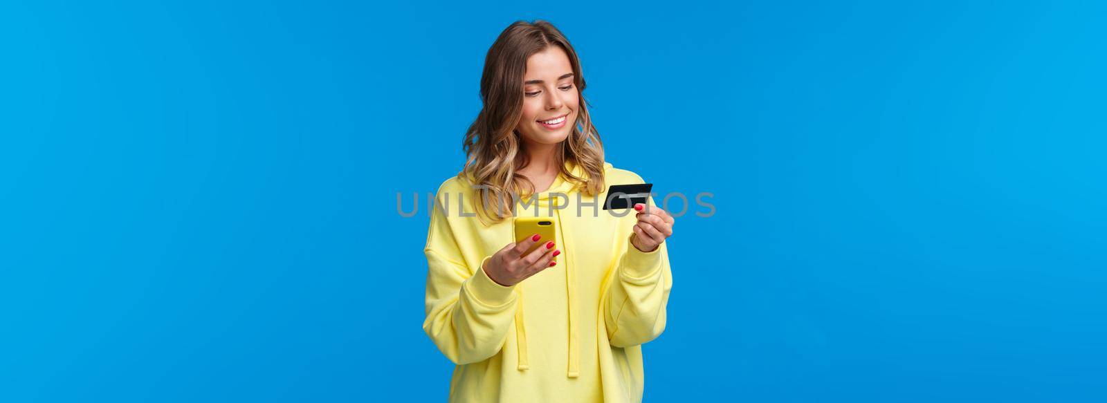 Young caucasian female with blond short hair using mobile phone and insert digit numbers of credit card to pay for her online purchase, shopping in internet store, smiling pleased by Benzoix