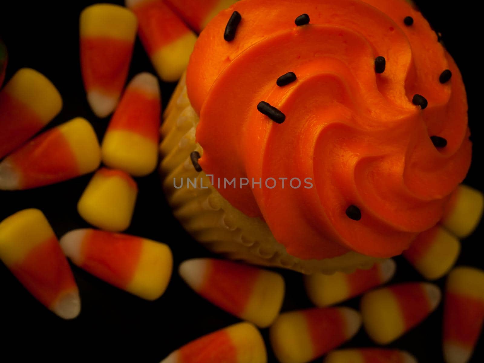 Halloween orange and black cupcakes with candy corn candies on black background.