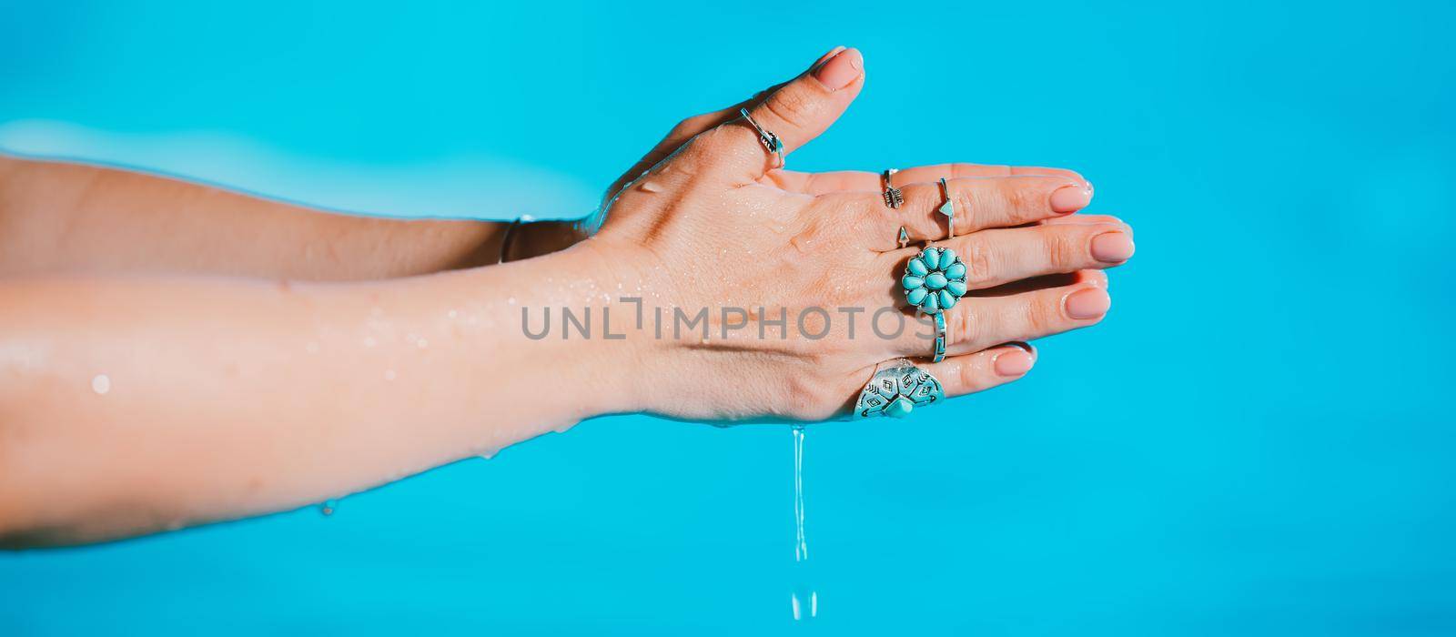 Priestess woman pours out clean water. Palms with gypsy boho rings holding clear aqua. Meditation, praying, gratitude, purity background. High quality photo