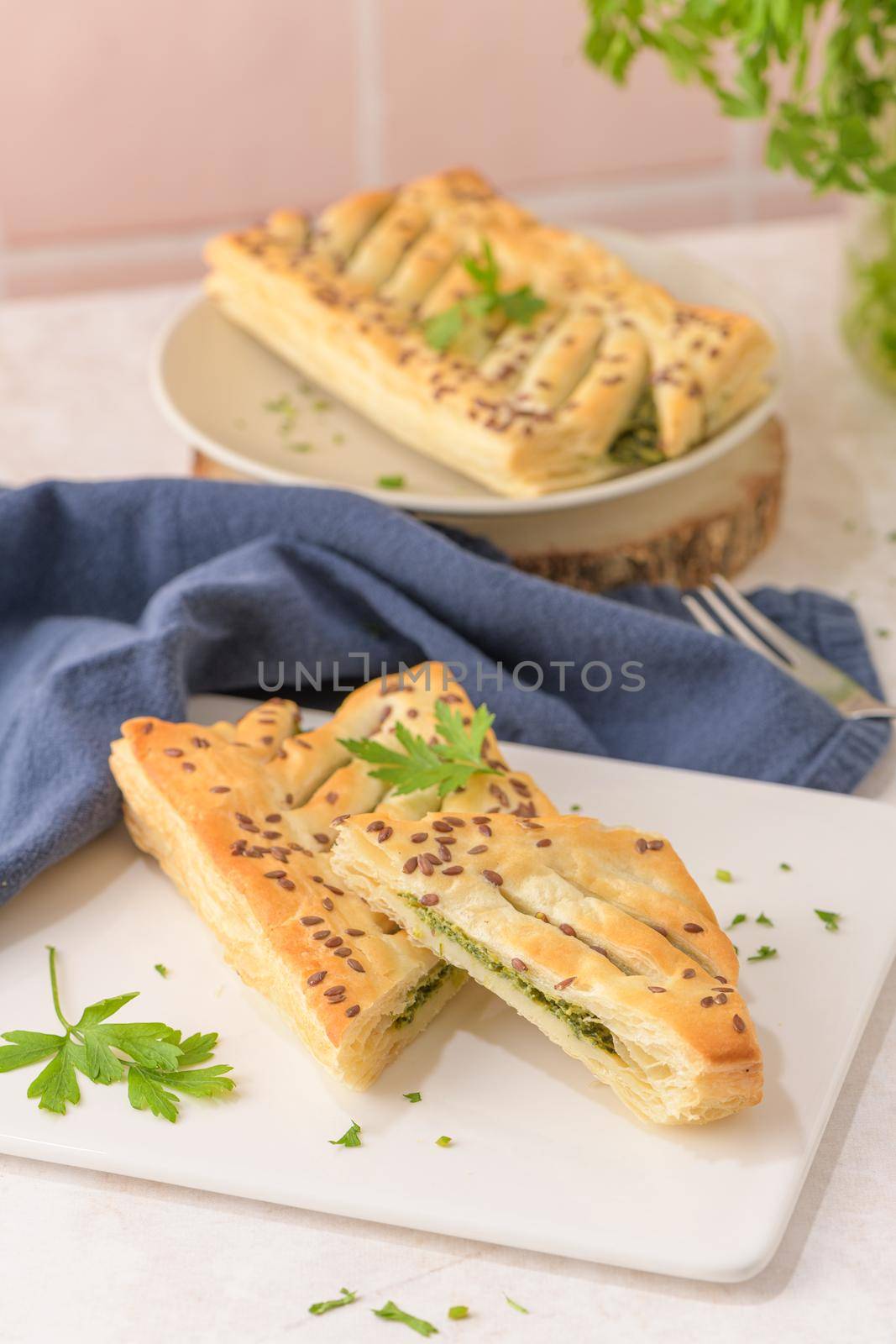 Spinach puff pastry with ricotta cheese and parsley leaves on white ceramic dishes in a kitchen counter top.