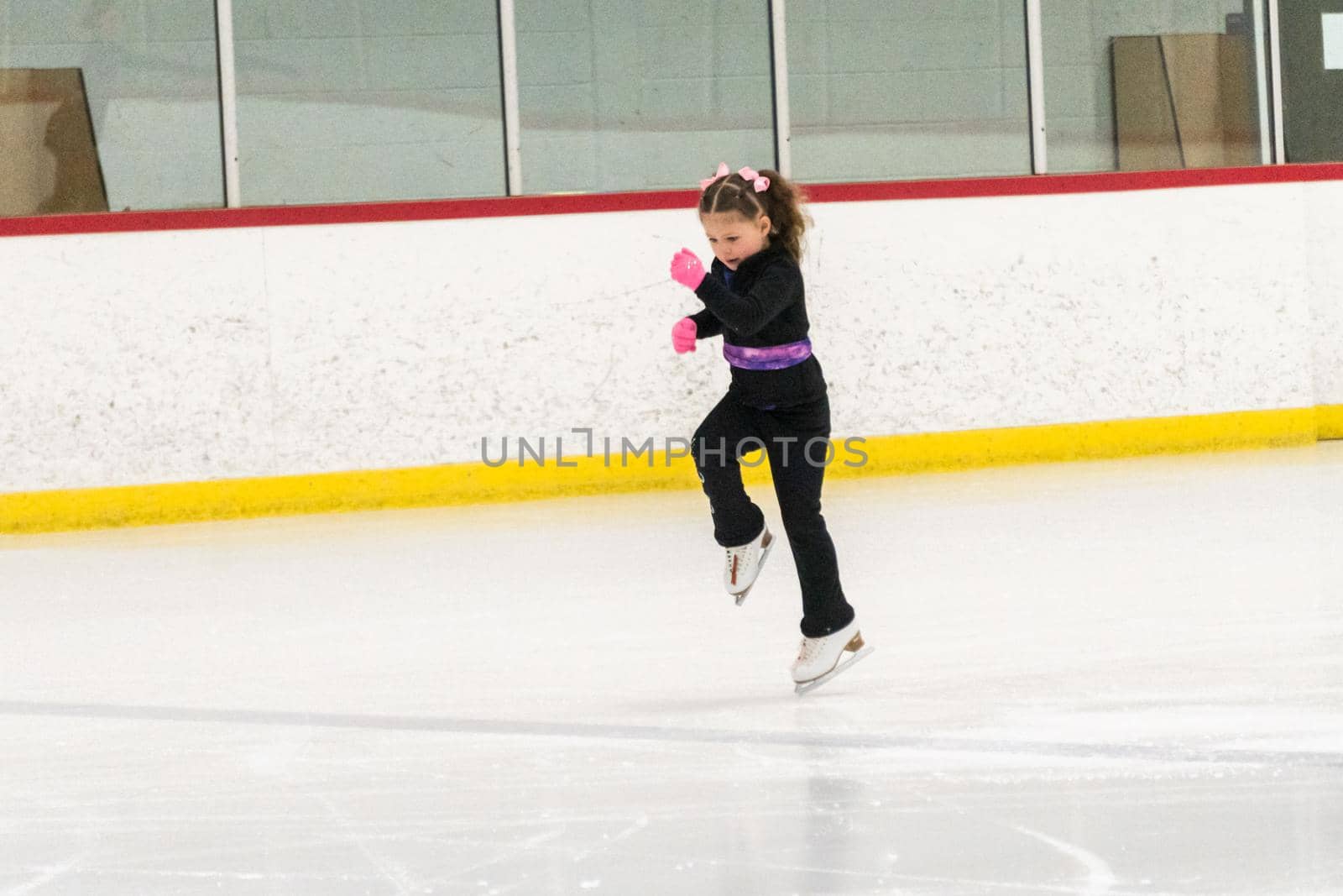 Little girl practicing figure skating moves on the indoor ice rink.