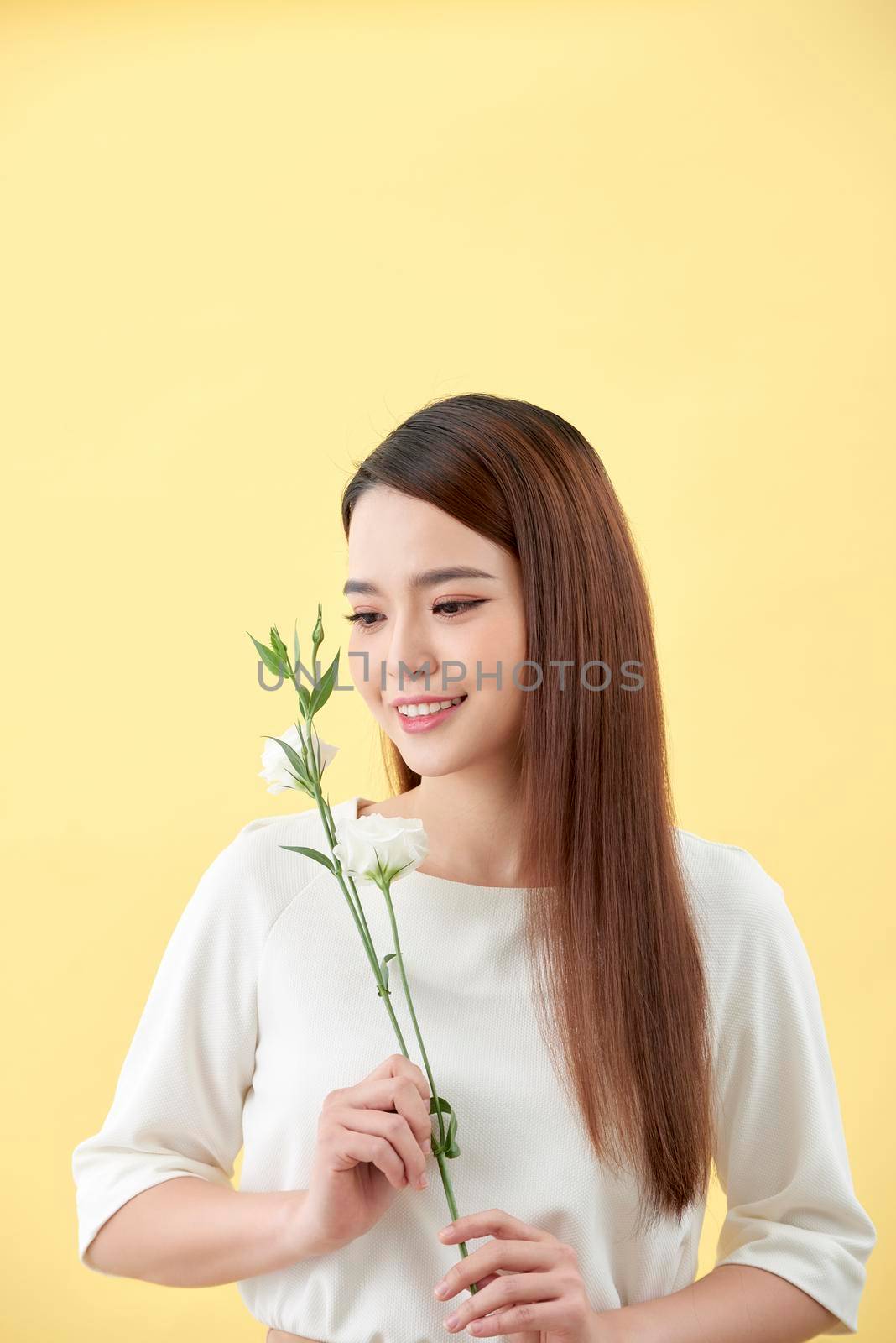 Beauty portrait of lady 20s holding white lisianthus flowers over yellow background by makidotvn