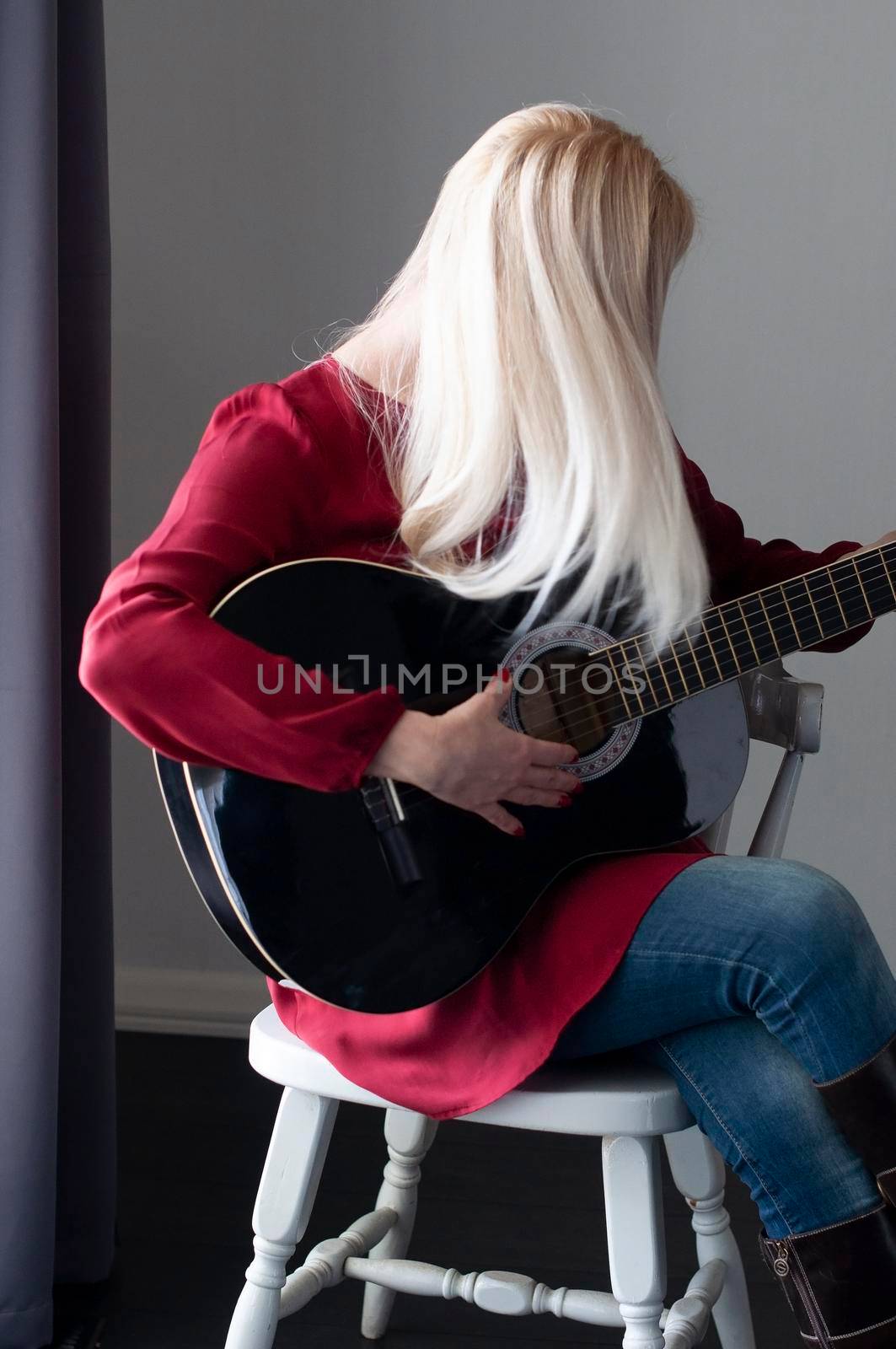 beautiful young blonde woman in a red dress with a black guitar, favorite hobby, music project. High quality photo
