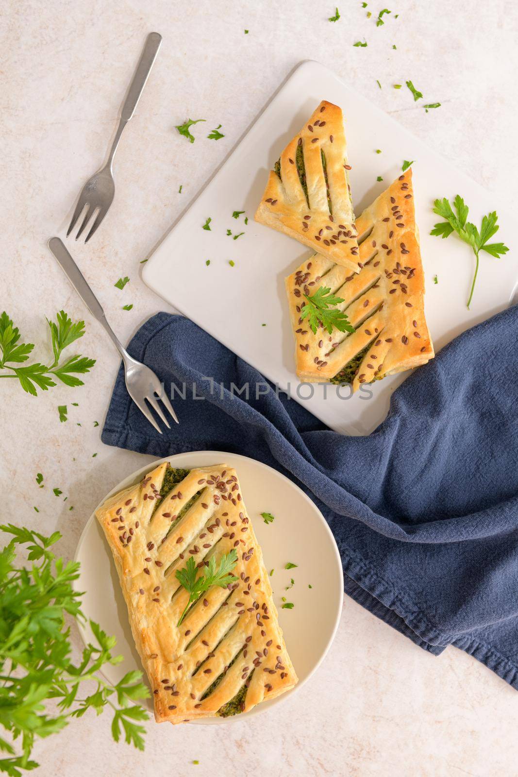 Spinach puff pastry with ricotta cheese and parsley leaves on white ceramic dishes in a kitchen counter top.