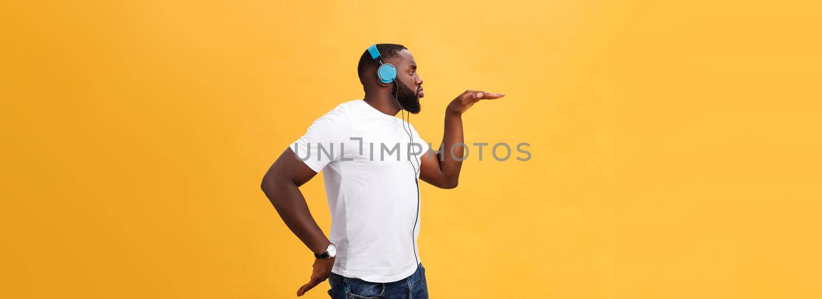 Young African American man wearing headphone and enjoy music dancing over yellow gold Background.