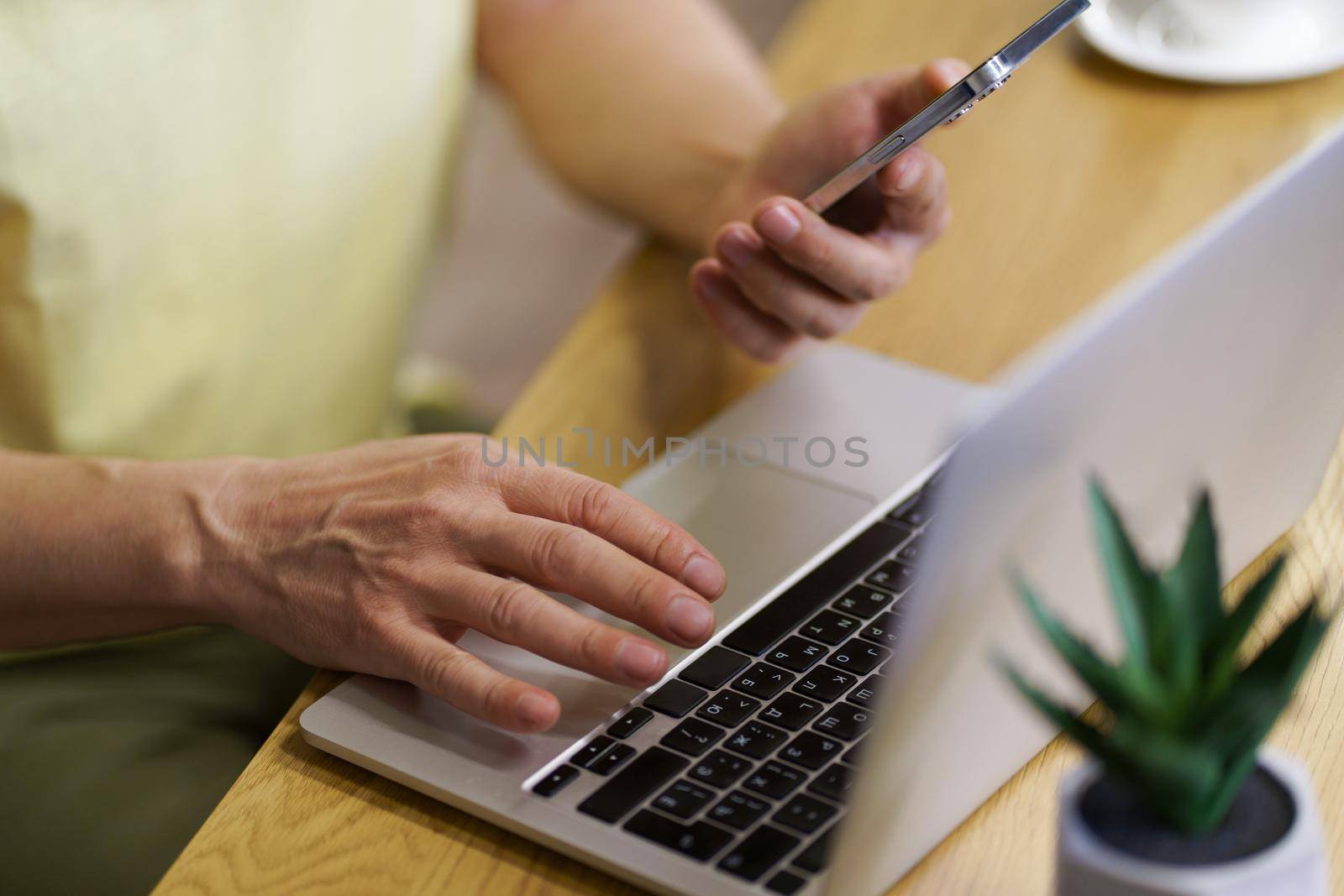 Technology and people lifestyle mans hand hold smartphone and working on laptop sitting at desk at home or office. Close up focus on mans hands working on computer. Businessman working on computer.