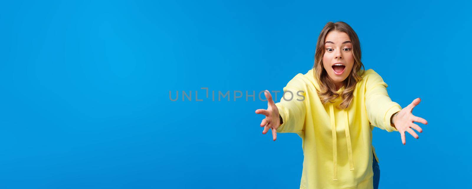 Girl trying to catch somthing, look focused and amused playing with kids, stretching hands and lean forward to read object with concentrated expression, standing blue background.