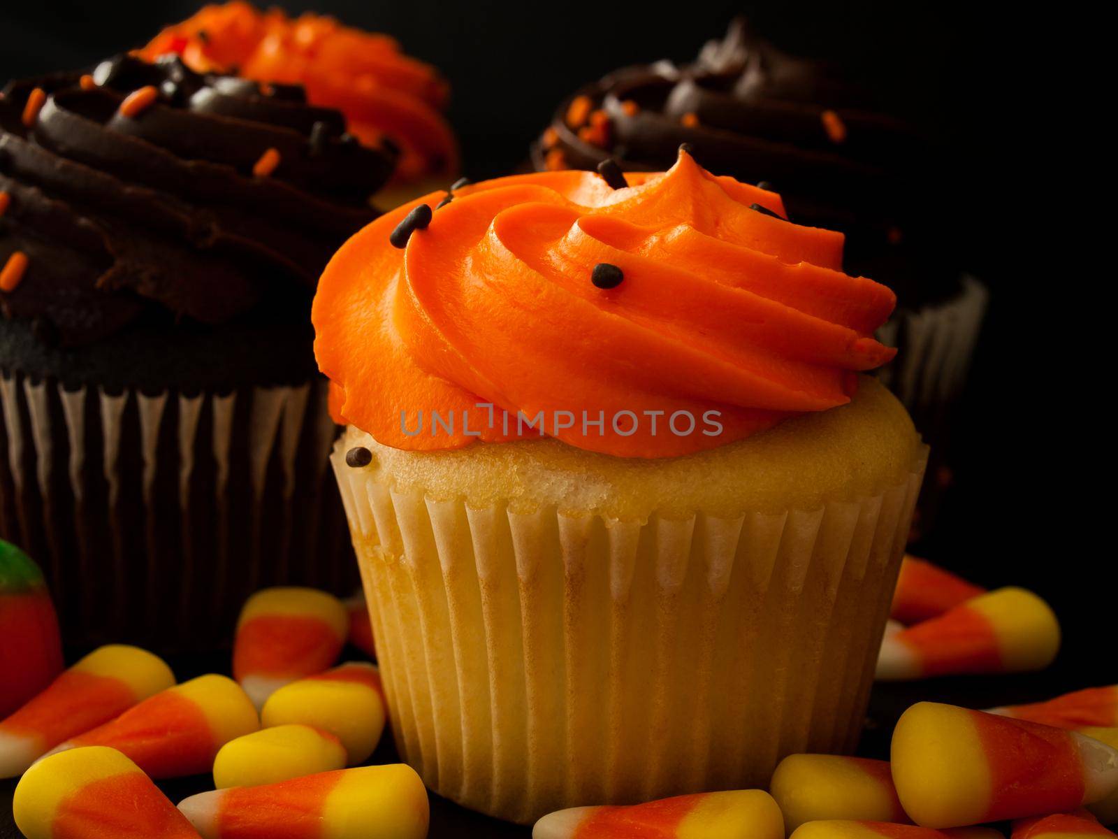 Halloween orange and black cupcakes with candy corn candies on black background.