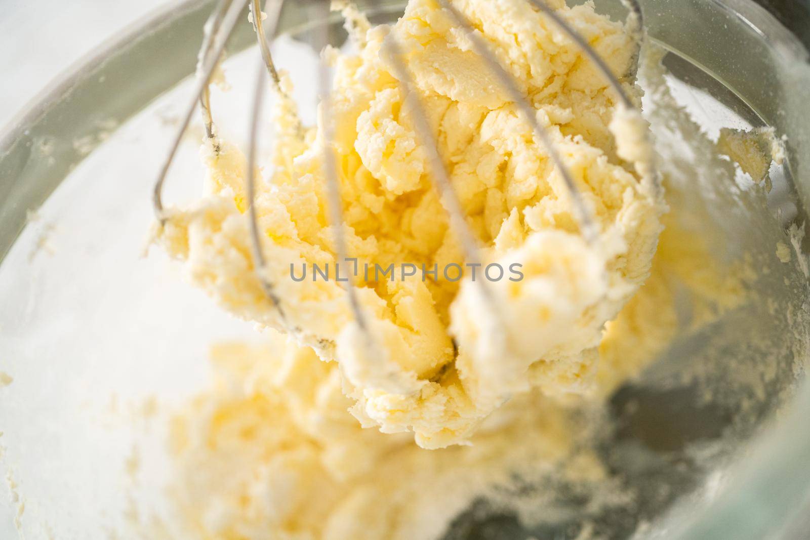 Mixing ingredients in a large glass mixing bowl of kitchen mixer to make eggnog buttercream frosting.