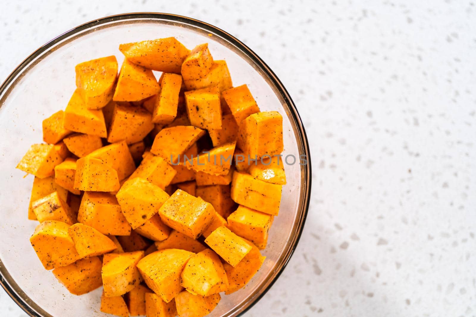 Seasoning cubed sweet potatoes to make oven-roasted sweet potatoes.