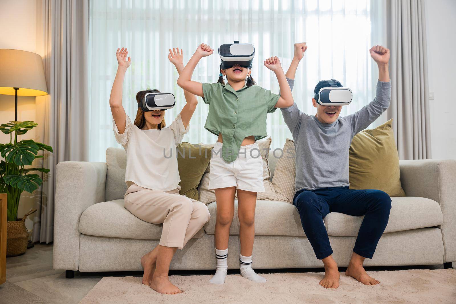 Asian family wear vr glasses headsets sitting on sofa in living room by Sorapop