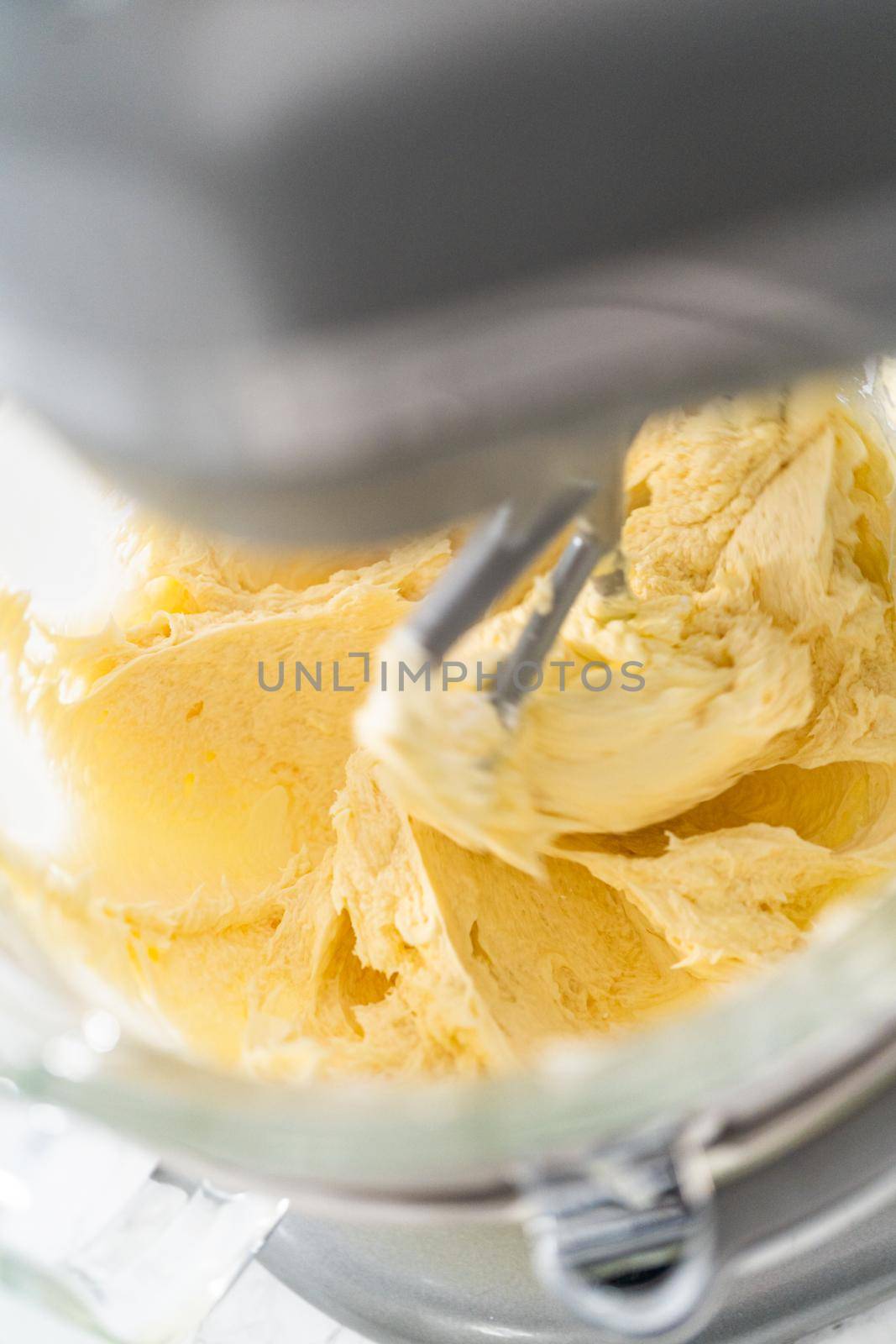 Whisking buttercream frosting in a glass mixing bowl with an electric kitchen mixer for American flag mini cupcakes.