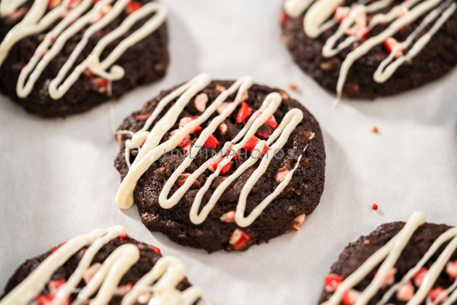 Freshly baked chocolate cookies with peppermint chips with a white chocolate drizzle on top.