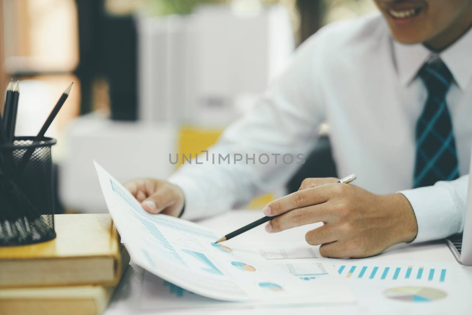 Young asian businessman working hard at the office using laptop data graphs, planning for improvement, snalyzing and strategizing for business growth. Business concept.