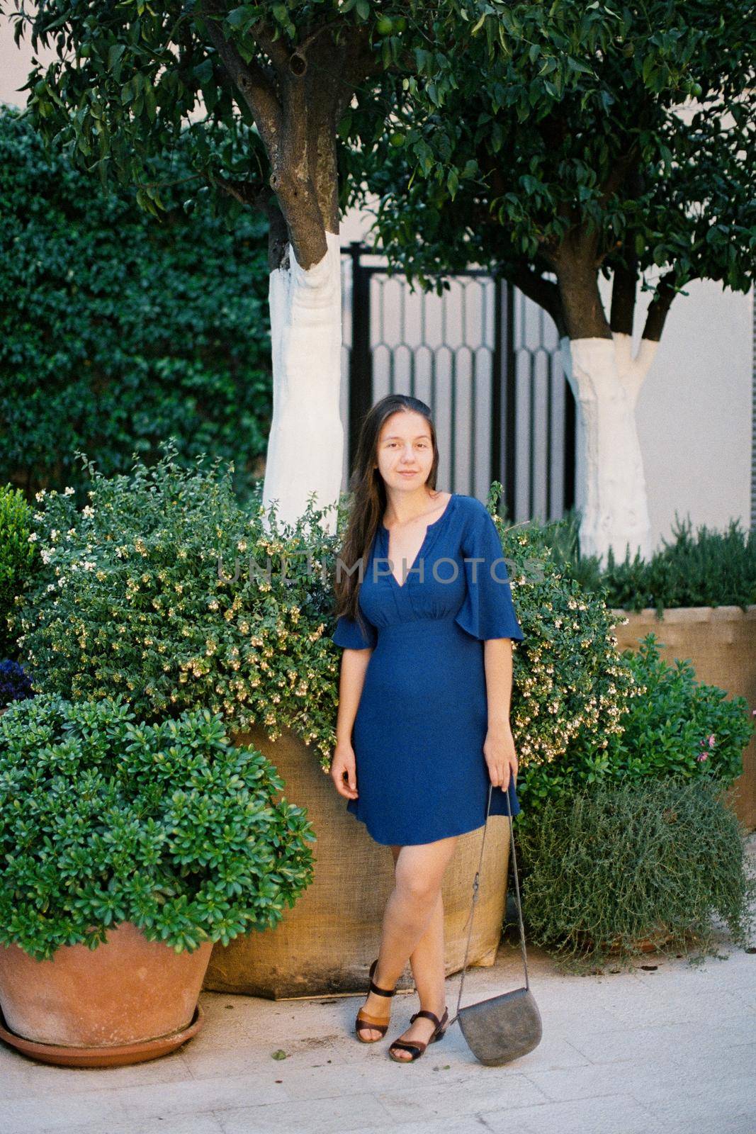 Young woman with a handbag stands near large flower pots in the garden. High quality photo