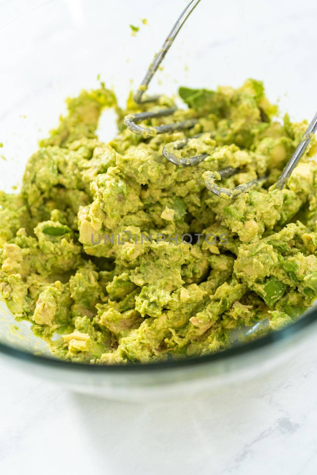 Smashing avocados in a glass mixing bowl to make classic guacamole dip.