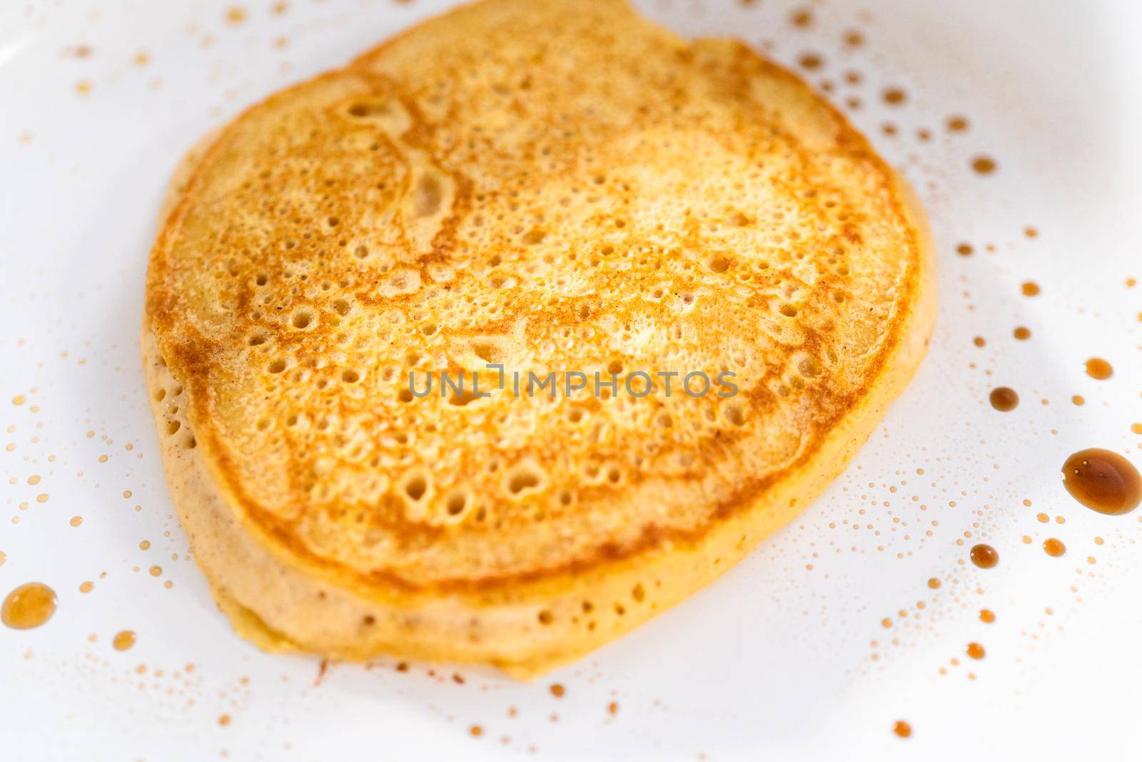 Frying pumpkin pancakes batter on a white frying pan.