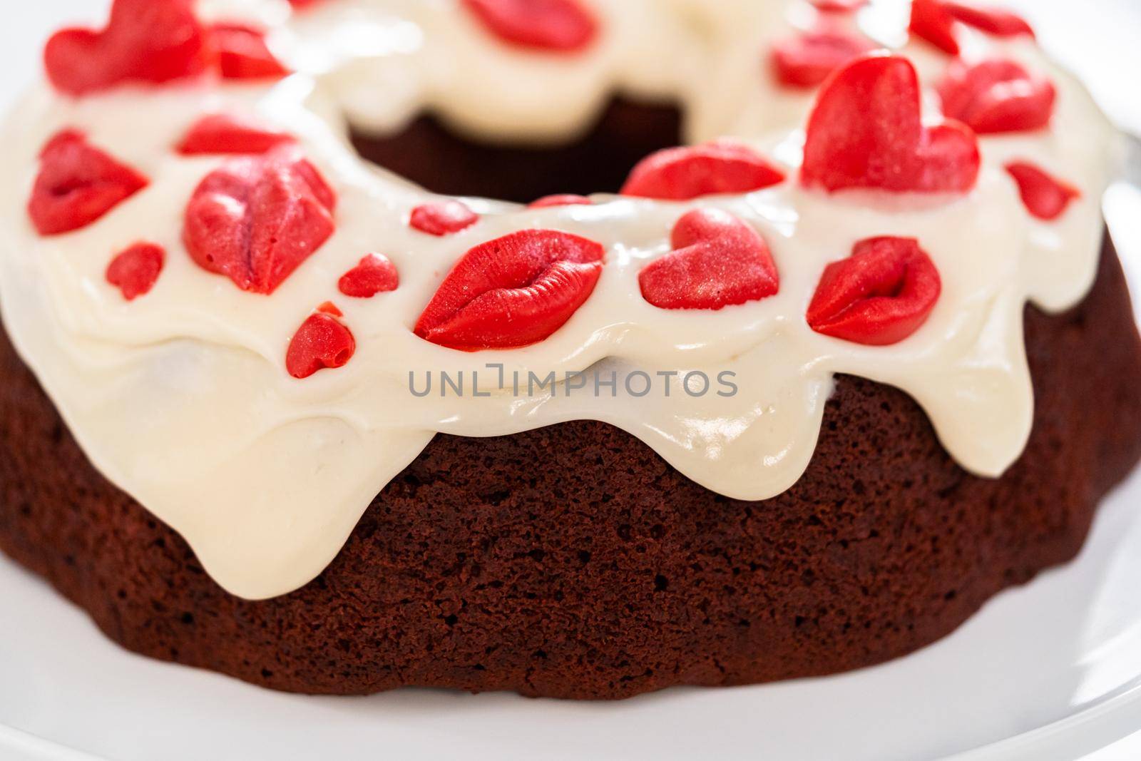 Freshly baked red velvet bundt cake with chocolate lips and hearts over cream cheese glaze for Valentine's Day.